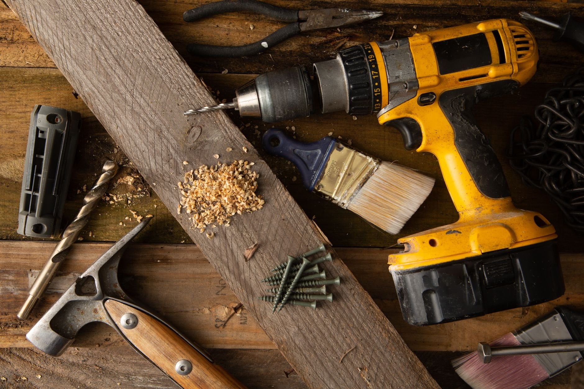 A close-up of various tools including a drill, hammer, and paintbrush on a wooden workbench.